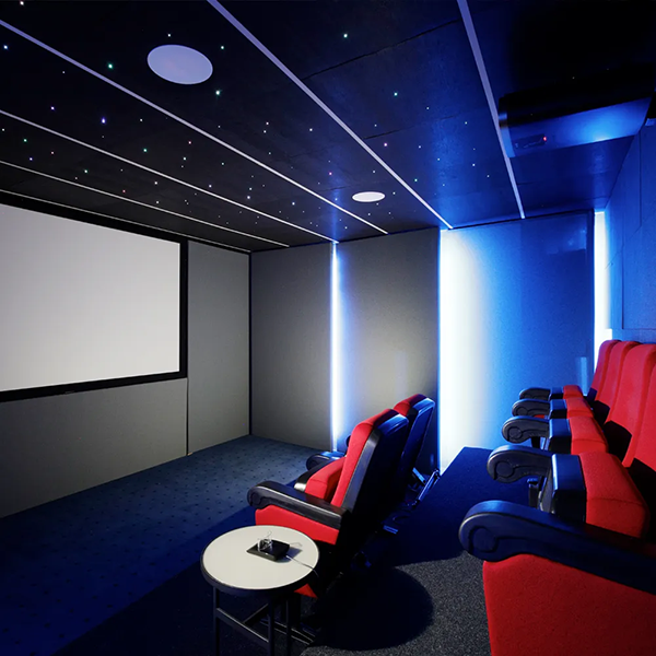 Kleiner Kinoraum mit indirektem kaltem Licht im Hintergrund. Auf der rechter Bildseite befinden sich die roten Kino-Sitzplätze und auf der linken Seite die eingebaute Kinoleinwand
