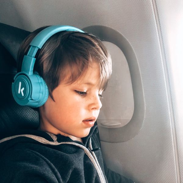 Kleiner Bub im Flugzeug mit blauen Kekz-Kopfhörer