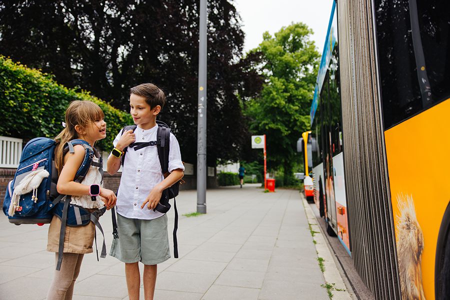 Zwei Schulkinder warten auf dem Bus mit Xplora Smartwatches