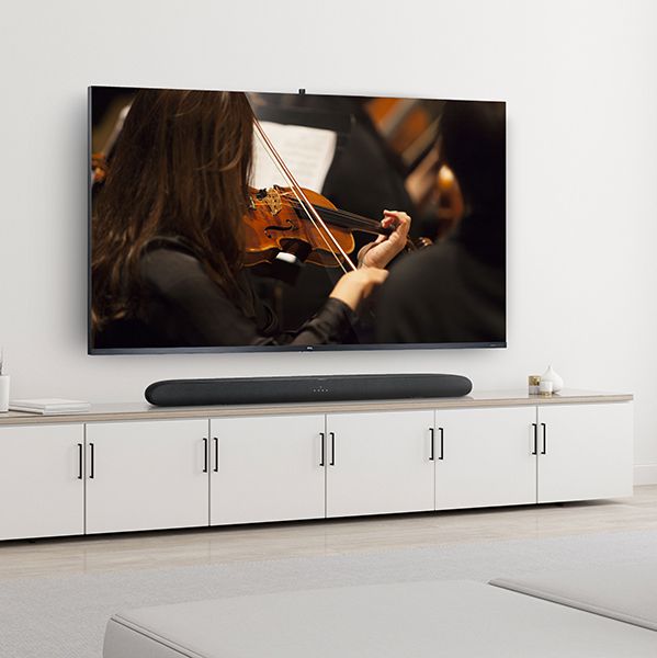 Weisses Zimmer mit weissem TV-Möbel und ein grosser TCL-TV im Fokus, der eine Geigenspielerin von der hinteren Seite abbildet