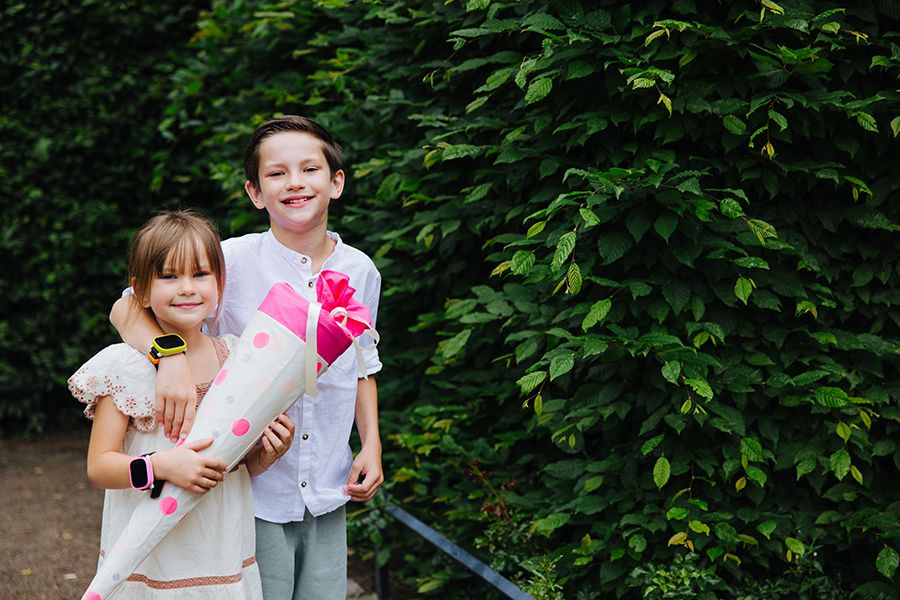 Zwei Schulkinder posieren vor einem Gebüsch, das Mädchen hält eine Schultüte