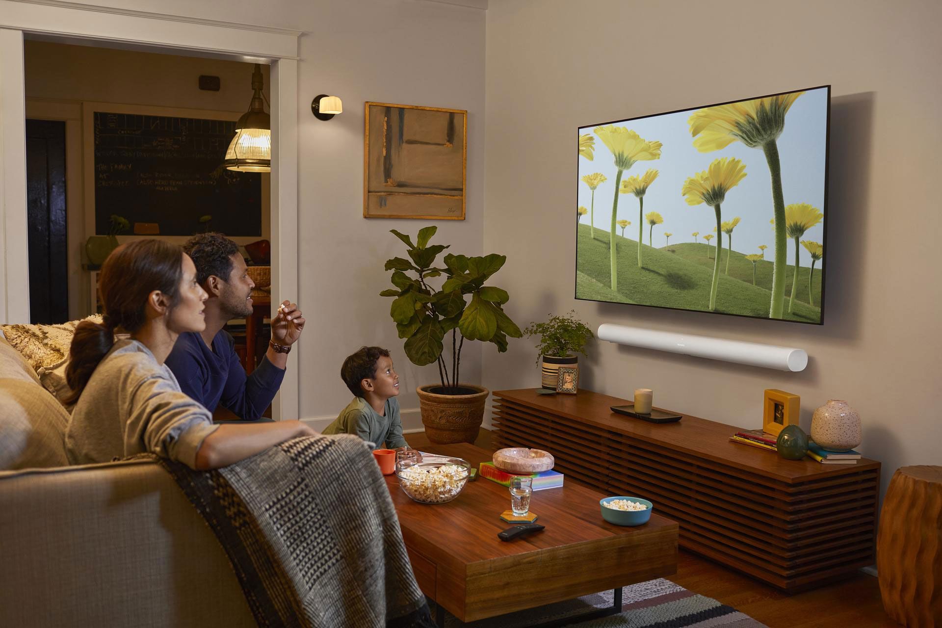 Fröhliche Familie sitzt zusammen im Wohnzimmer und schaut zusammen TV. Das Sounderlebnis kommt von der Sonos Arc unter dem TV.